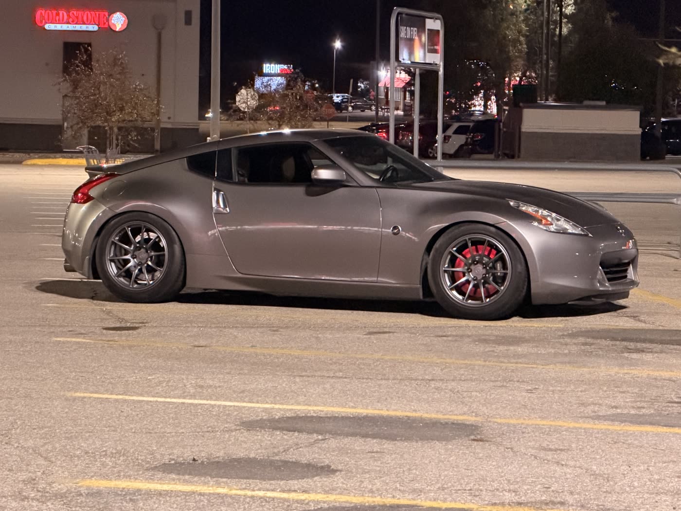 A gray Nissan 370Z on aftermarket wheels with red brake calipers, parked in a lot at night