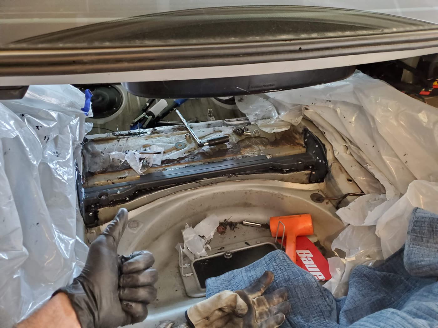 A gloved thumbs-up beside a new reinforcement plate fitted across the M3's trunk floor