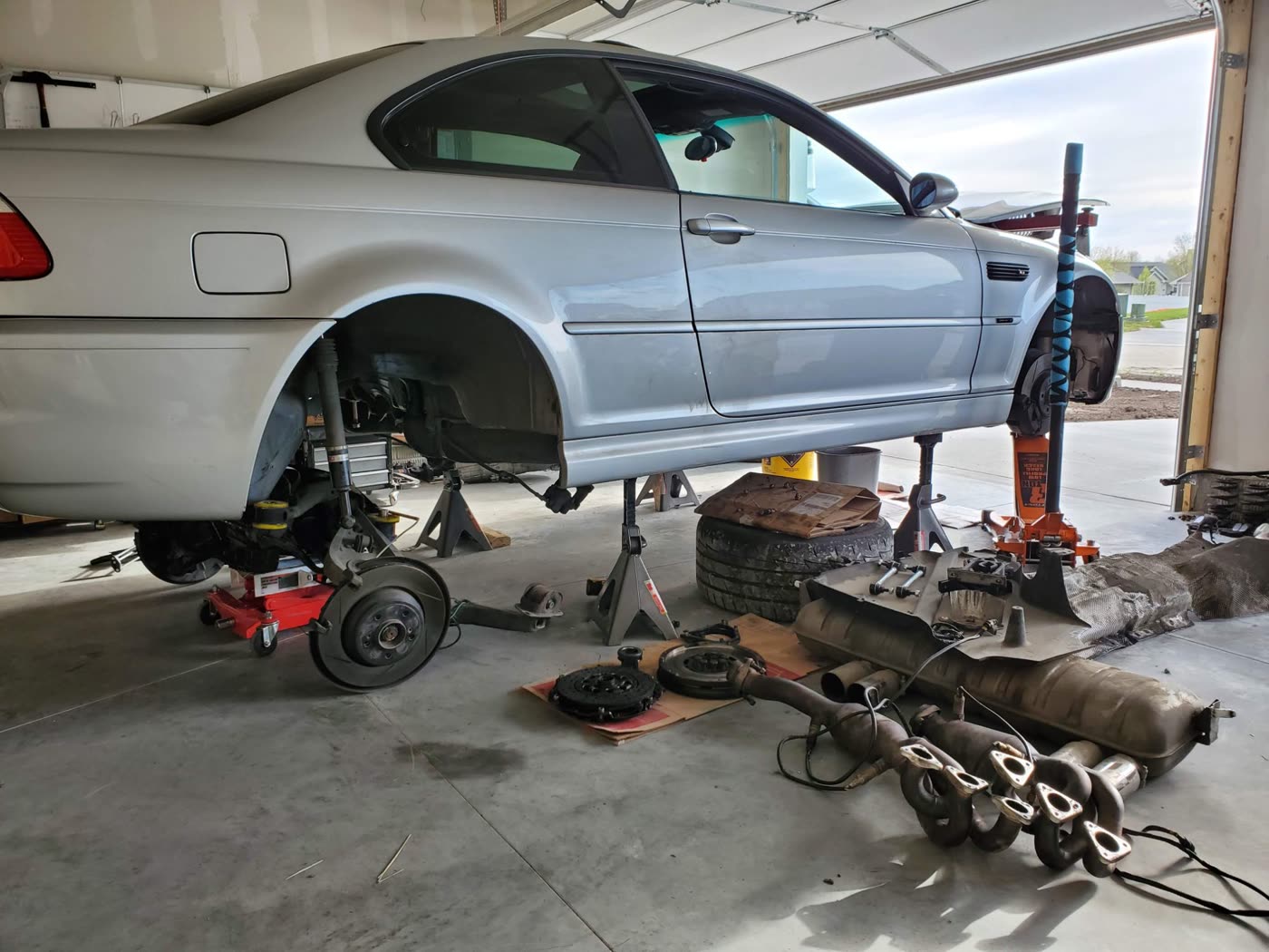 The E46 M3 on jack stands in a home garage, with its rear subframe, clutch, flywheel and exhaust on the floor