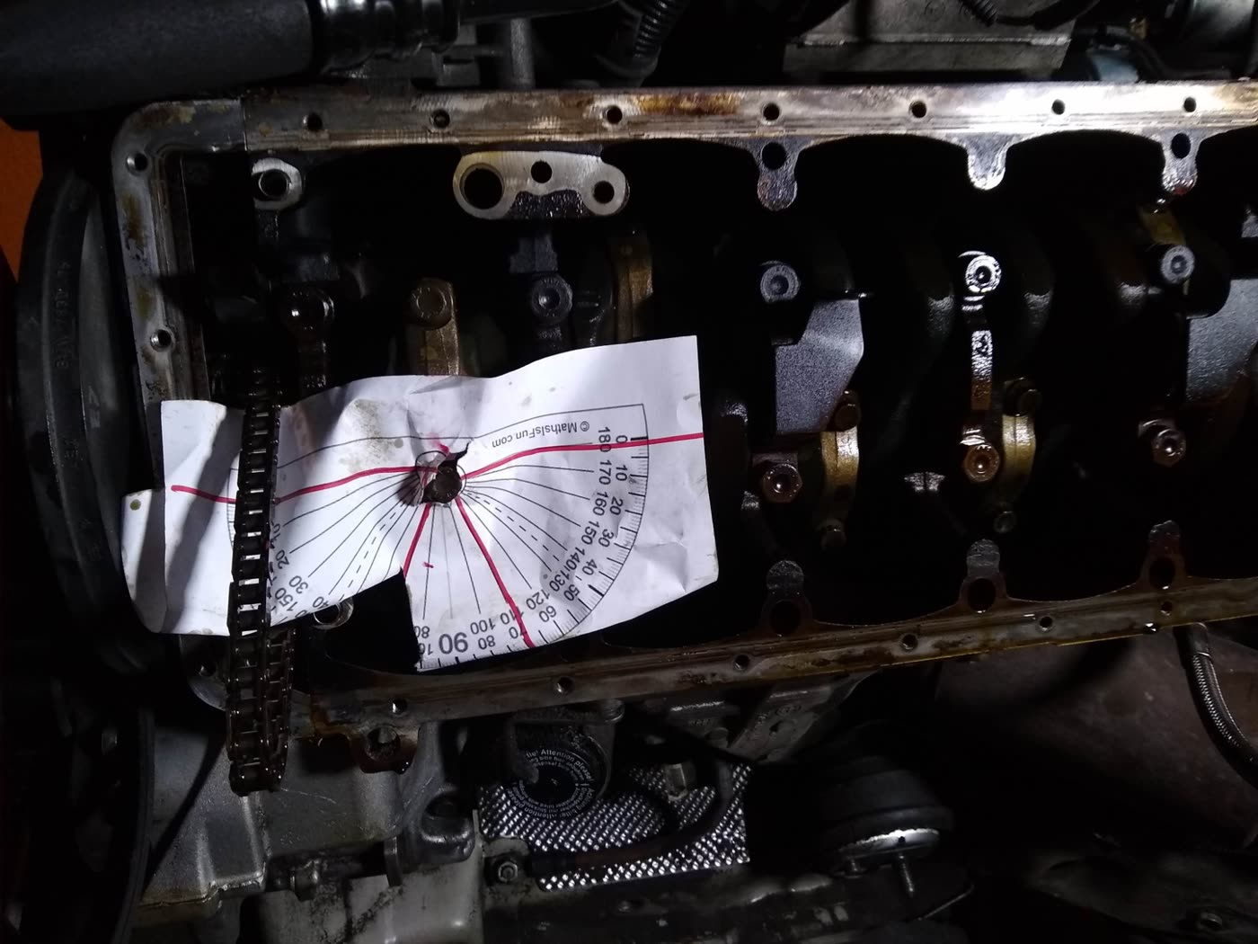 A printed paper protractor, marked in red pen, fitted over a bolt in the bottom of the engine