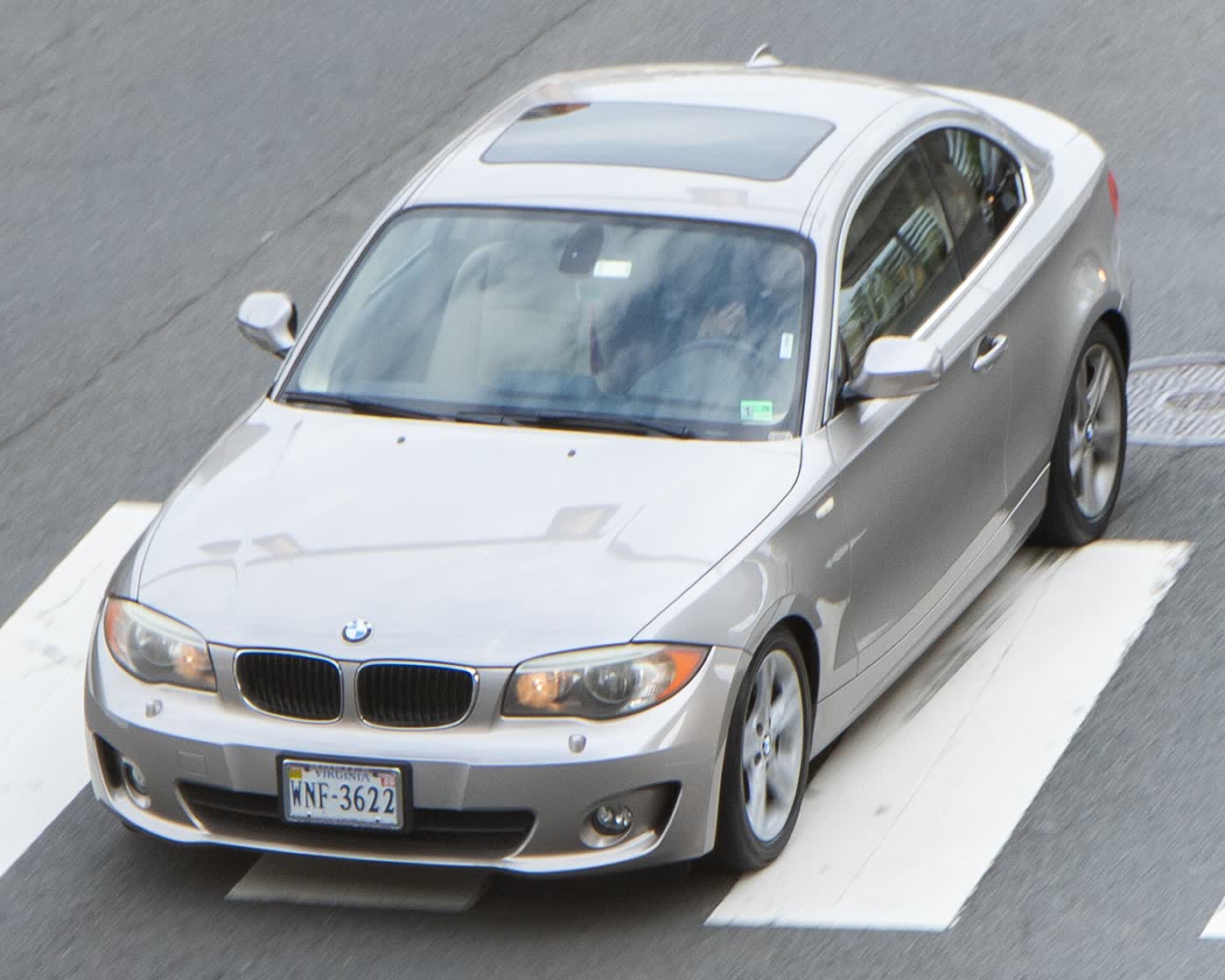 A silver BMW 128i E82 coupe driving on a road, seen from above and in front