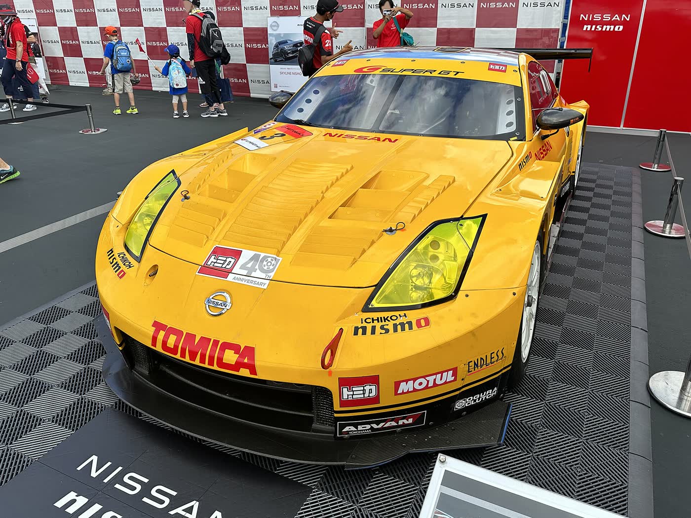 A yellow Nissan 350Z built for Super GT racing, with a large front splitter and rear wing, on display