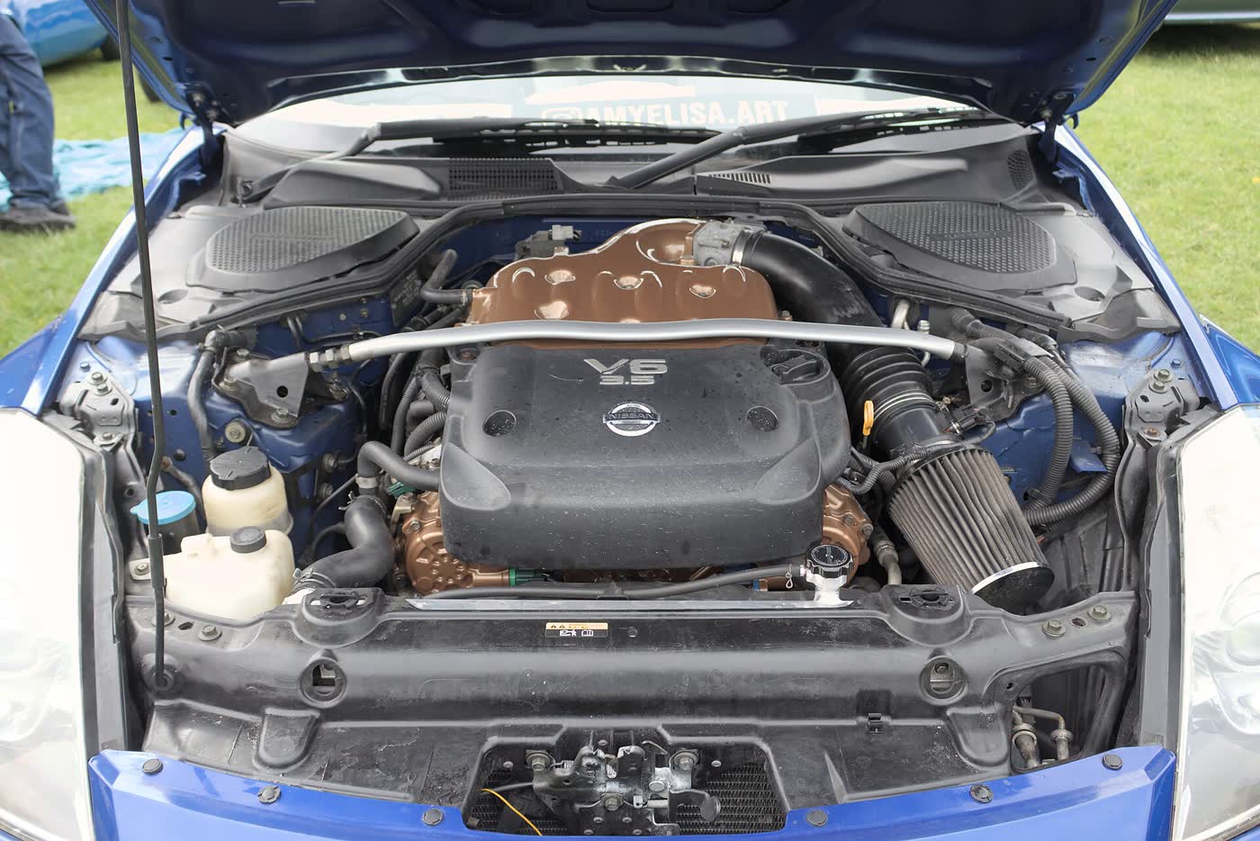 The engine bay of a Nissan 350Z with the bonnet raised, showing the VQ V6 and strut brace