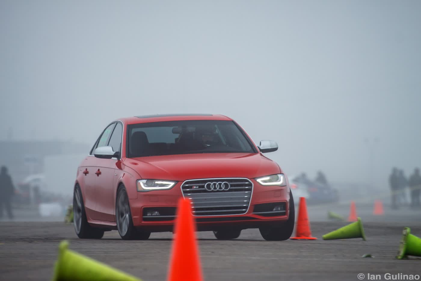 A red Audi S4 sedan with the facelift grille and LED headlights turning through traffic cones on a foggy autocross course