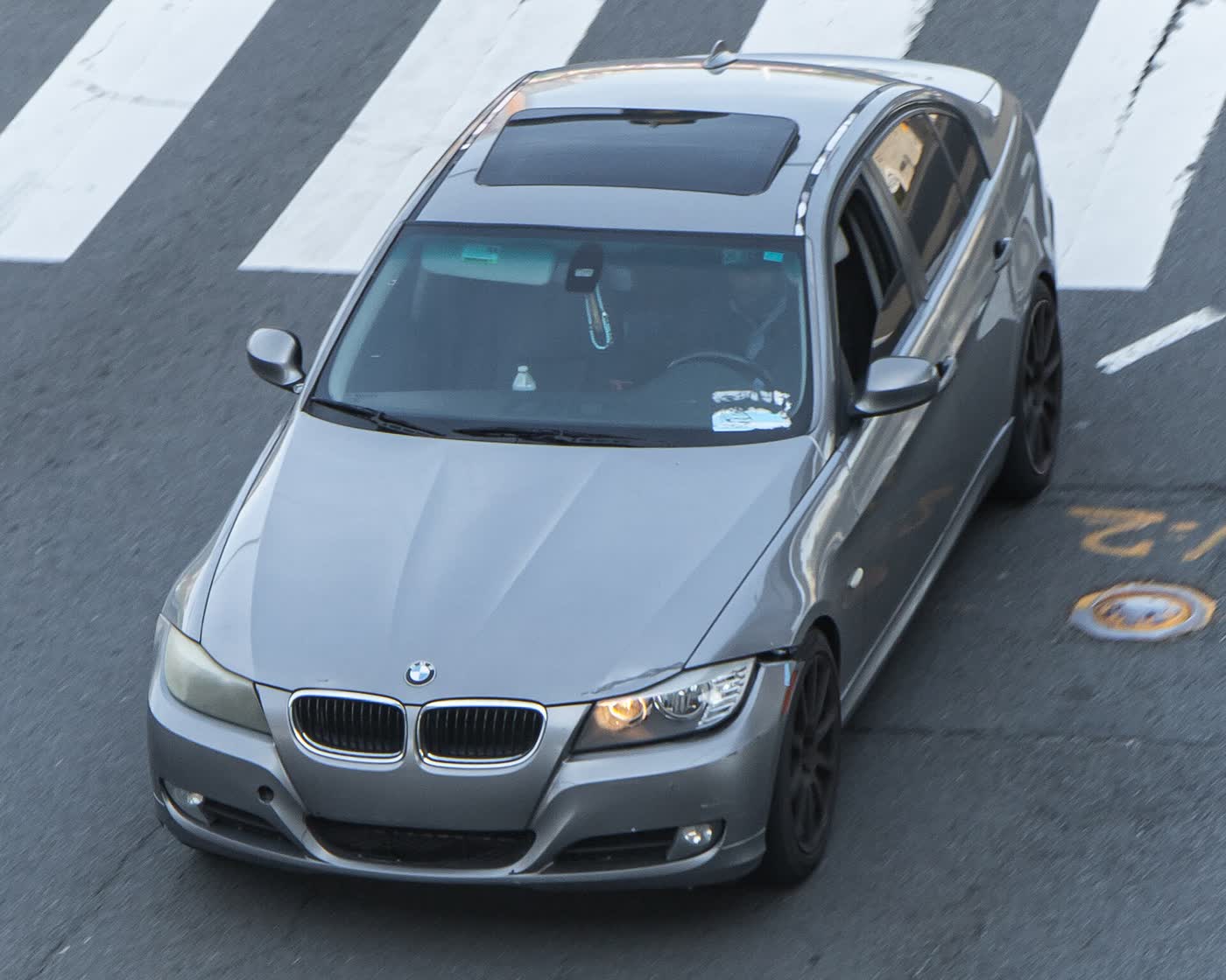 A grey BMW 335i sedan with dark wheels and a sunroof, seen from above as it crosses a painted crosswalk