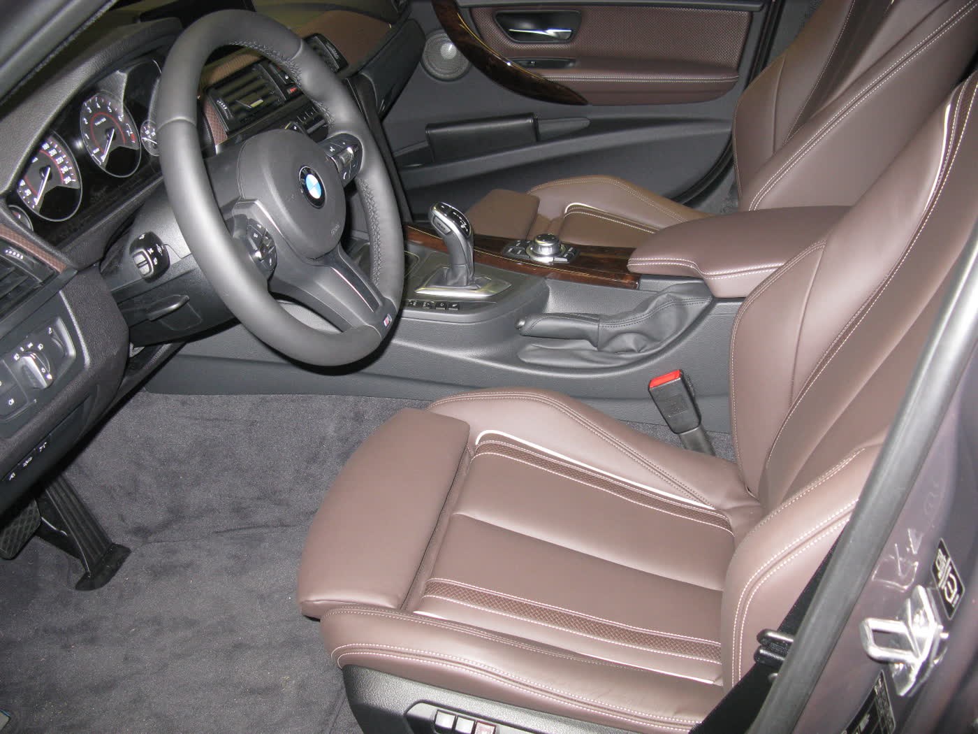 The front seats and dashboard of a BMW 335i Individual sedan, brown leather seats, an M-style steering wheel, wood trim and an automatic gear selector on the centre console