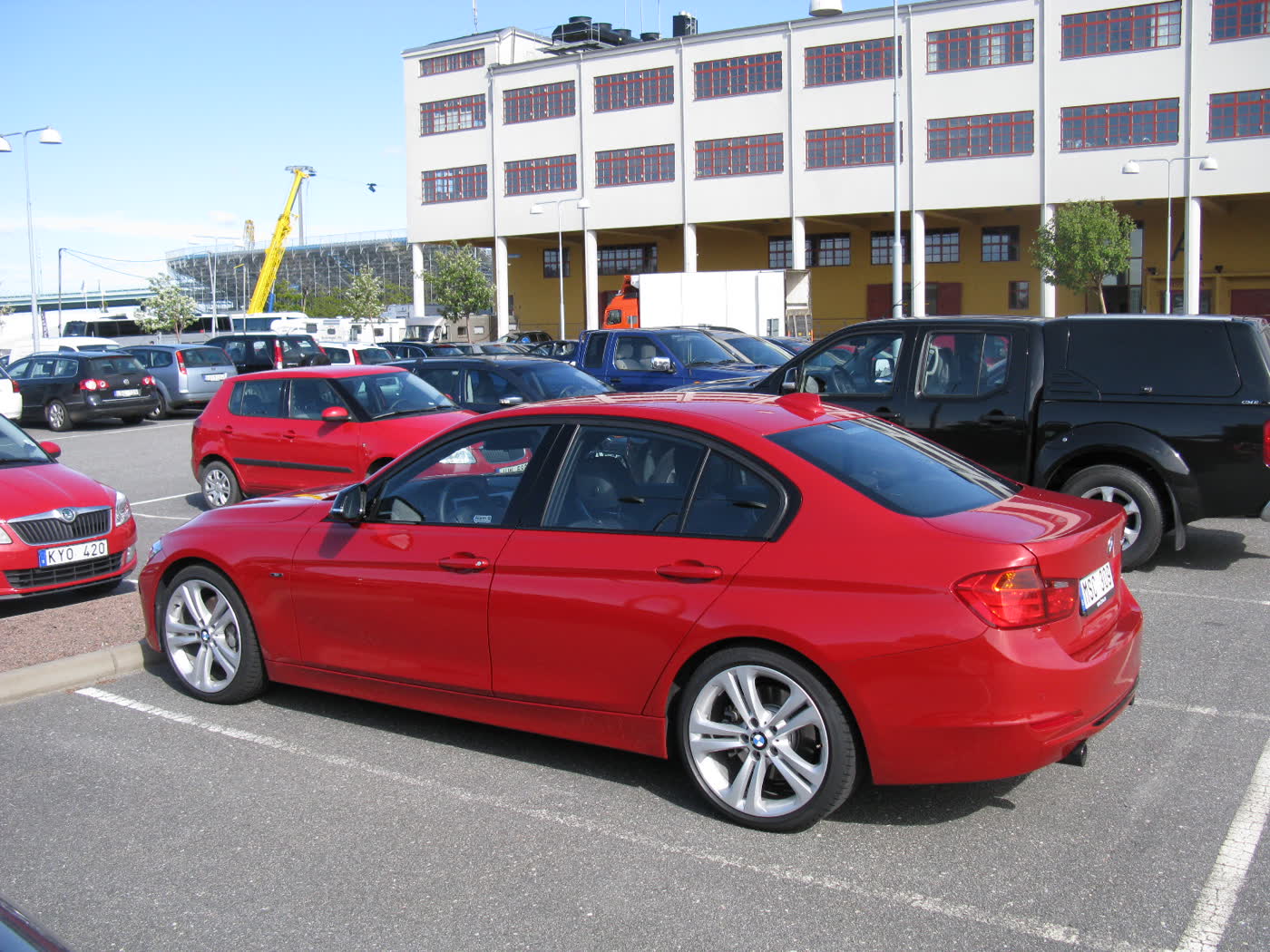 A red BMW 335i sedan of the F30 generation, rear three-quarter view, parked in a harbourside car park with buildings behind it