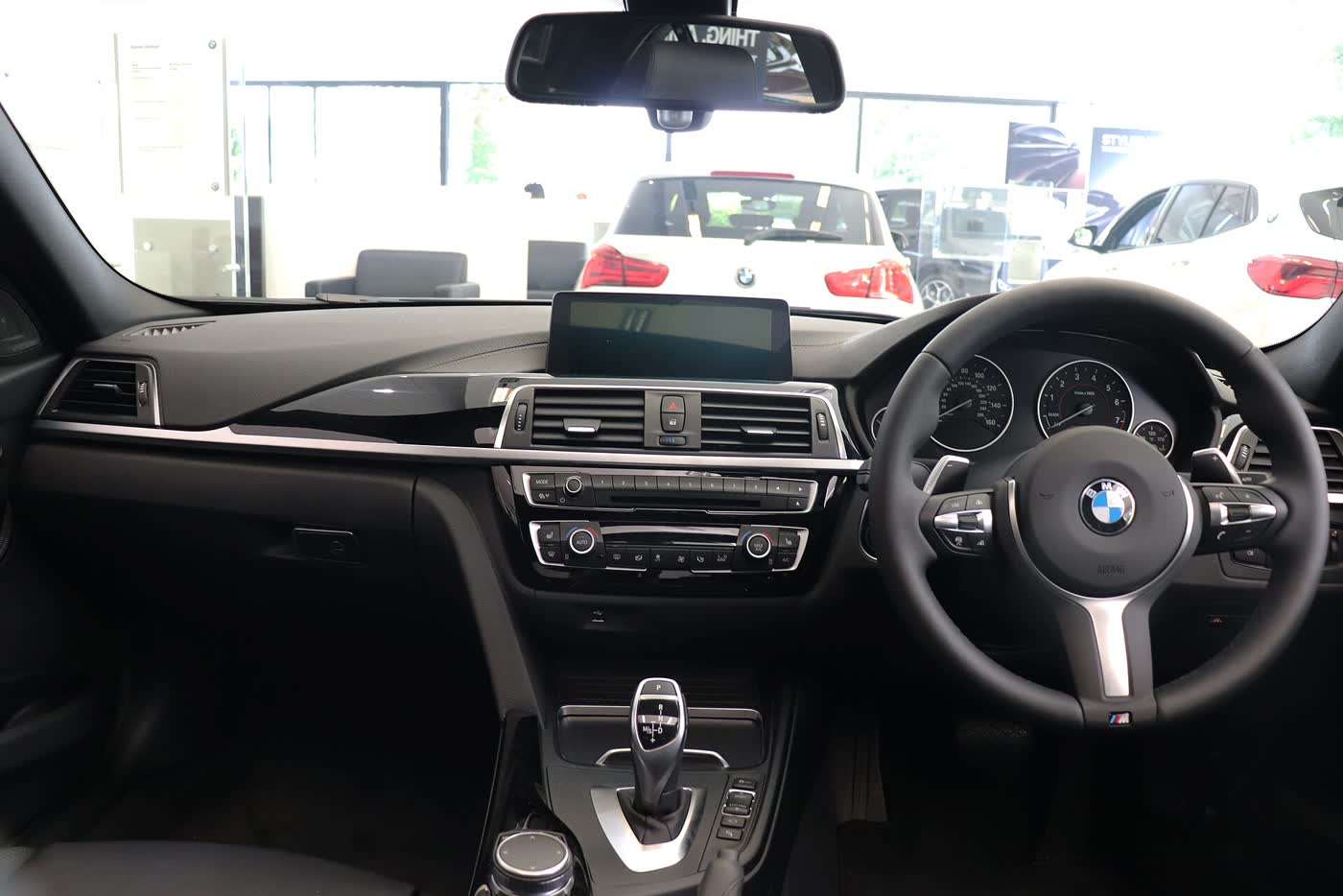 The dashboard of a BMW 340i M Sport from the driver seat, with a flat iDrive screen above the vents, an automatic gear selector on the console and an M steering wheel on the right-hand side