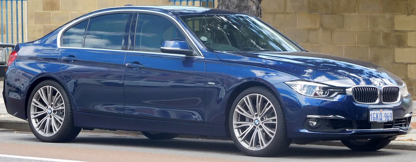 A dark blue BMW 340i Luxury Line sedan of the F30 facelift generation with silver multi-spoke wheels, side view, parked kerbside against a sandstone wall