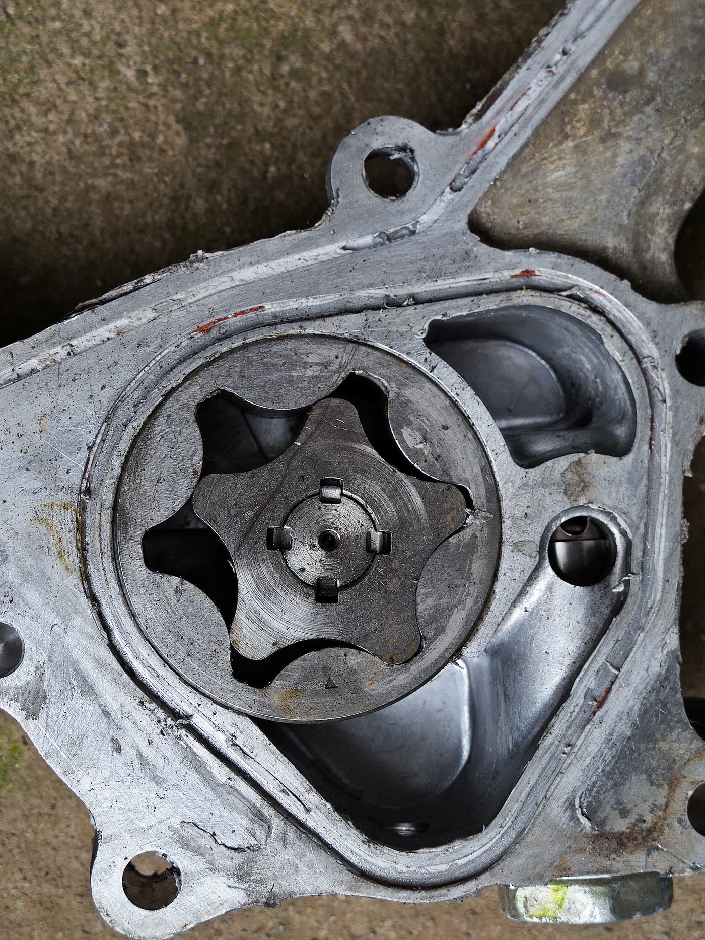 An opened engine oil pump housing in bare aluminium, showing a star-shaped inner rotor inside a lobed outer rotor