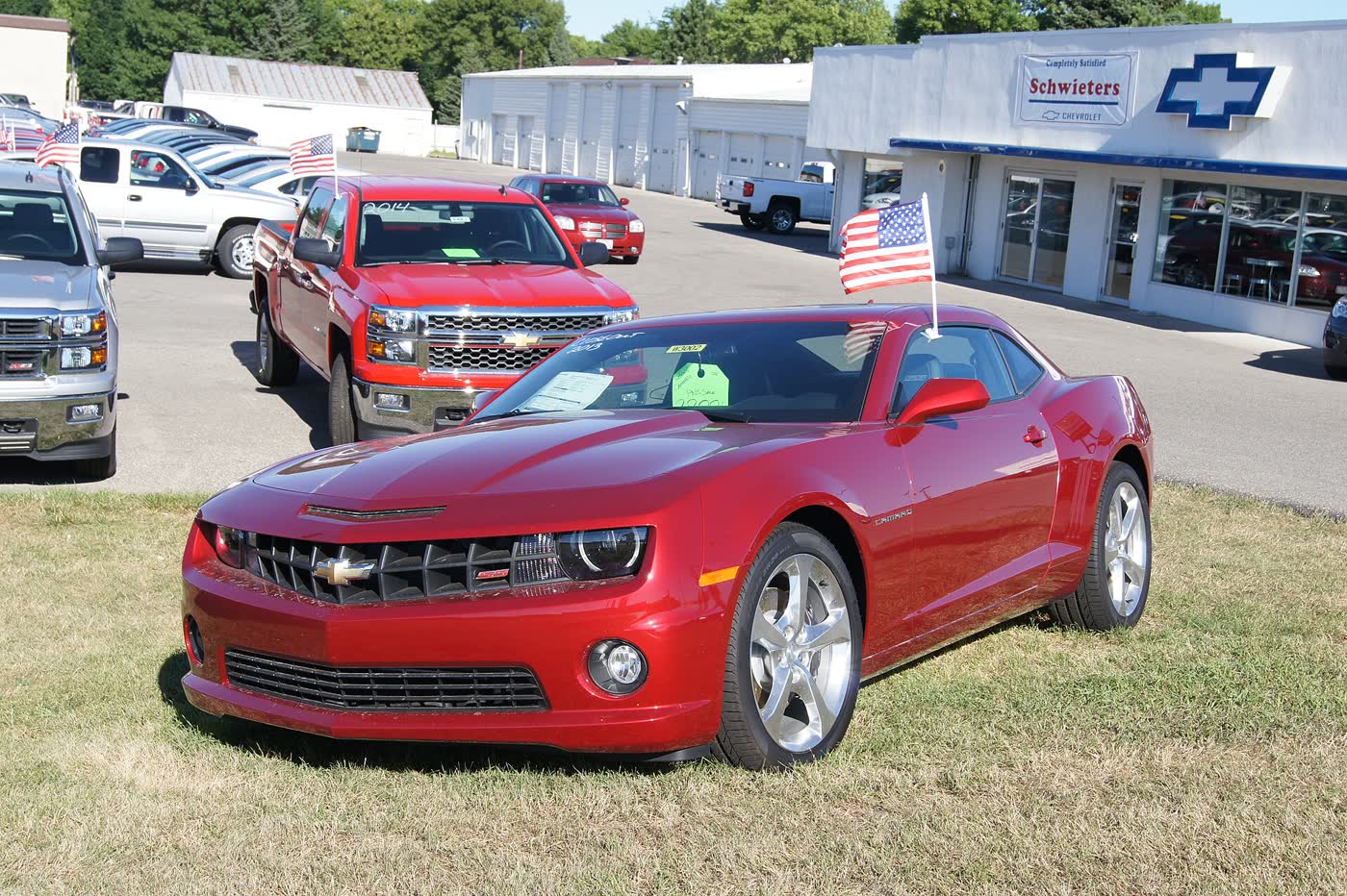 A crimson 2013 Chevrolet Camaro SS on a Chevrolet dealer lot with a window sticker in the glass