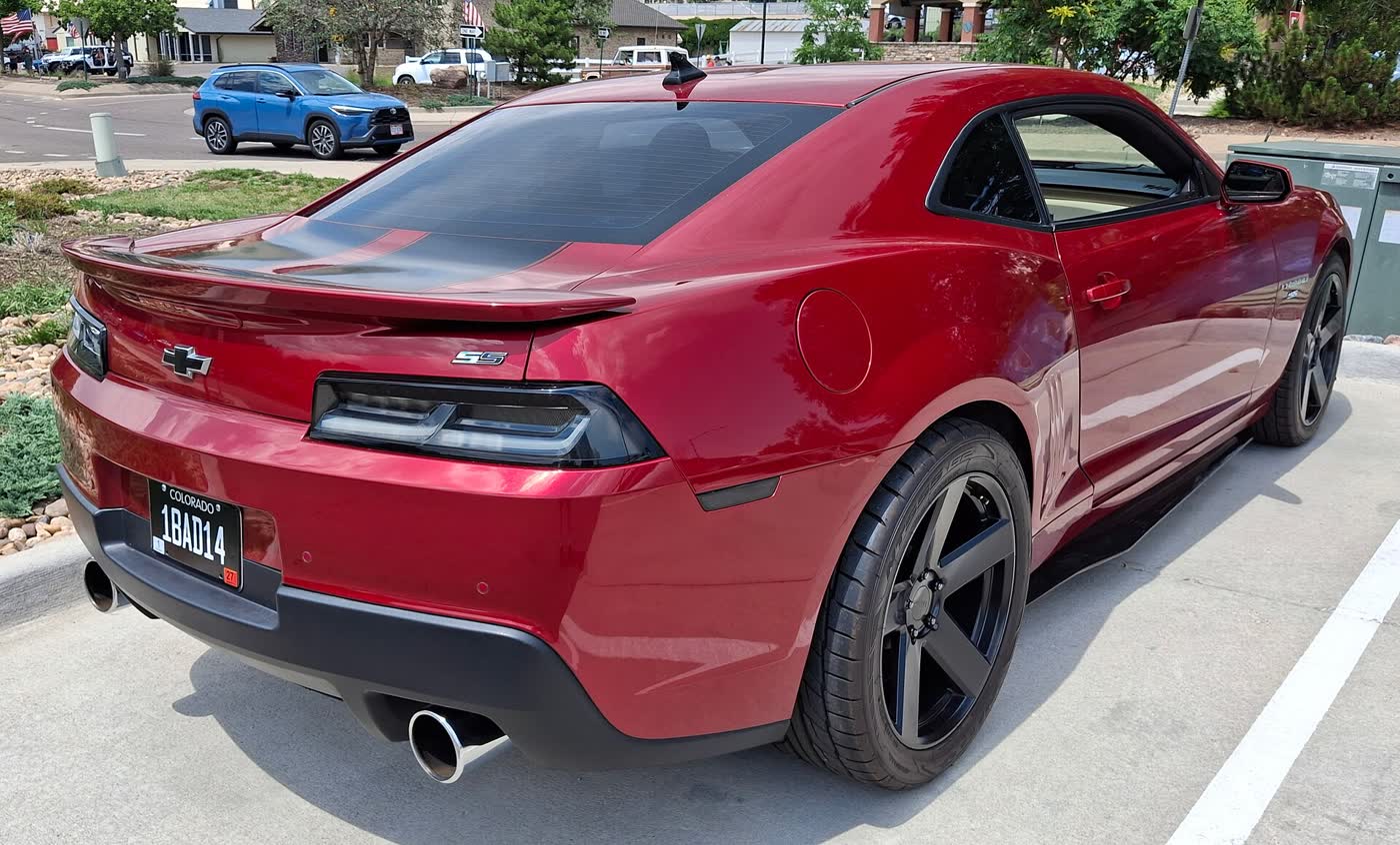 A dark red 2014 Chevrolet Camaro SS coupe from the rear three-quarter, SS badge on the tail and black wheels