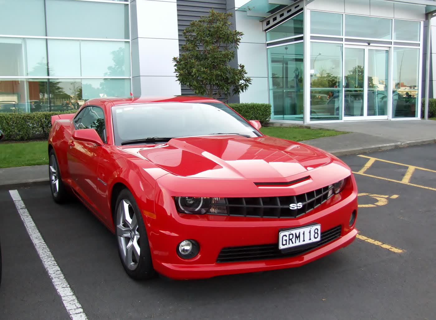 A red 2013 Chevrolet Camaro SS coupe, front three-quarter view, parked outside a glass building
