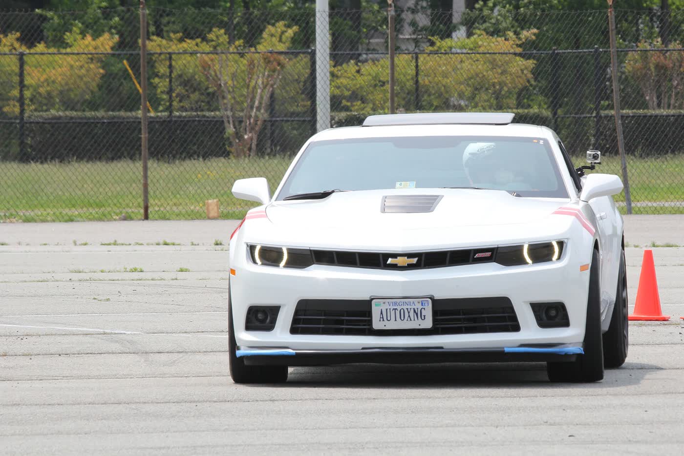 A white fifth-generation Chevrolet Camaro SS on an autocross course, helmeted driver inside and a cone beside the front wheel