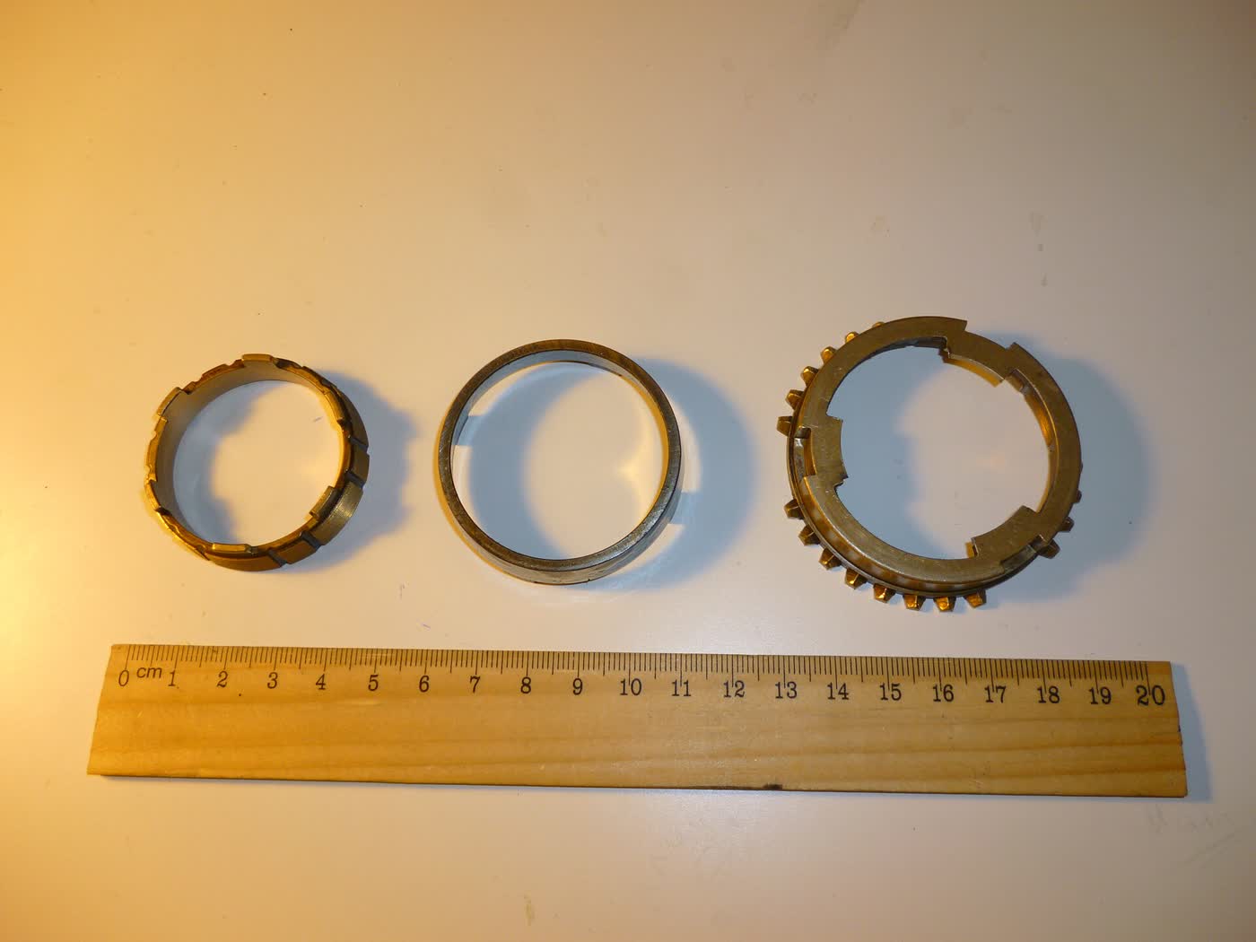 Three gearbox synchroniser rings laid on a bench beside a ruler for scale