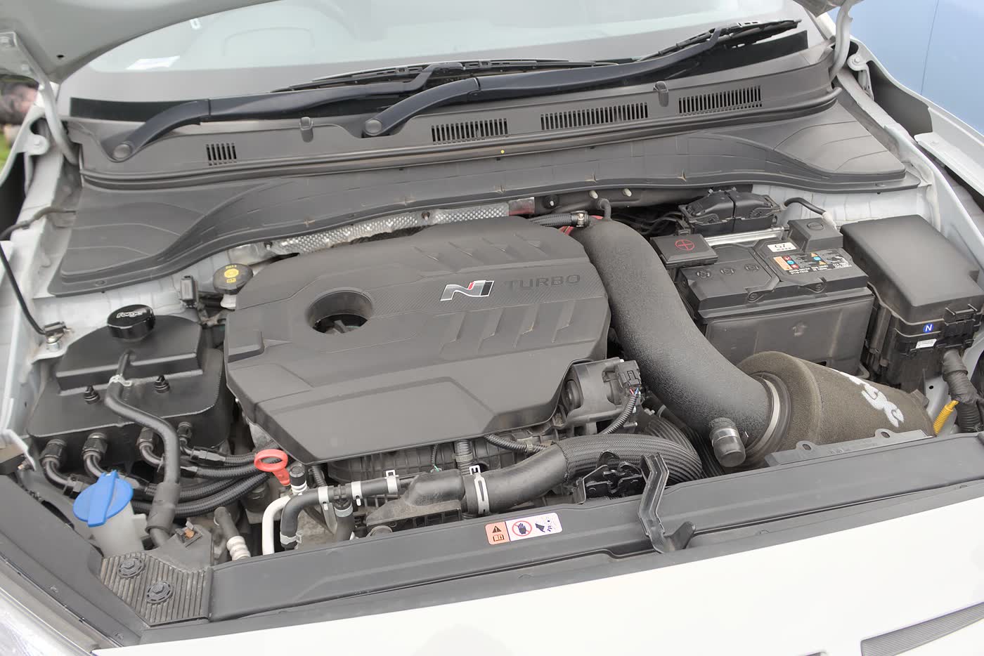 An open engine bay showing a transverse four-cylinder turbo engine under a black cover with an N logo, and a large intake duct running across it