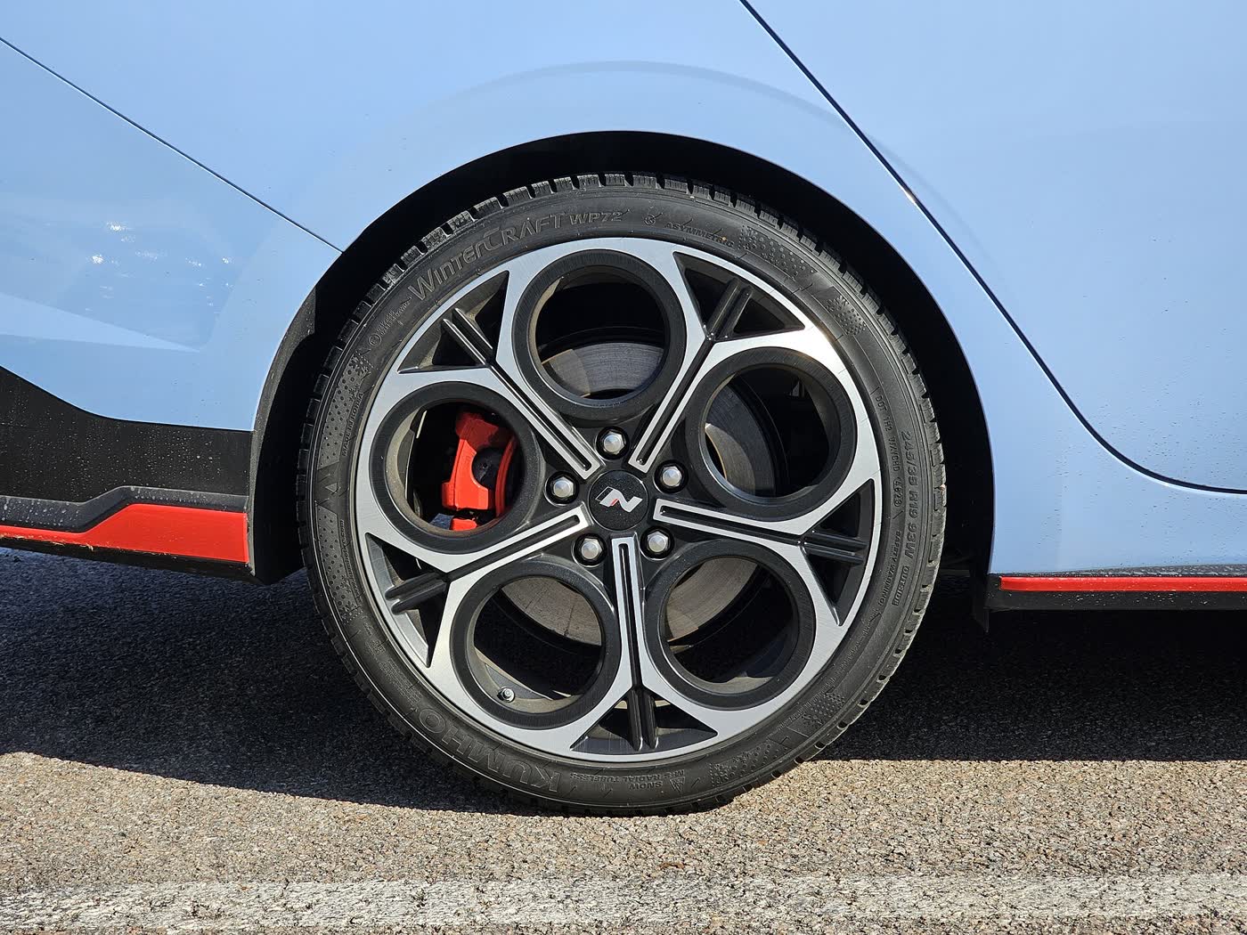 Close-up of the rear wheel of a light blue Hyundai sedan: a multi-spoke alloy wheel, a red brake caliper and a 245/35R19 winter tire, with red trim along the sill