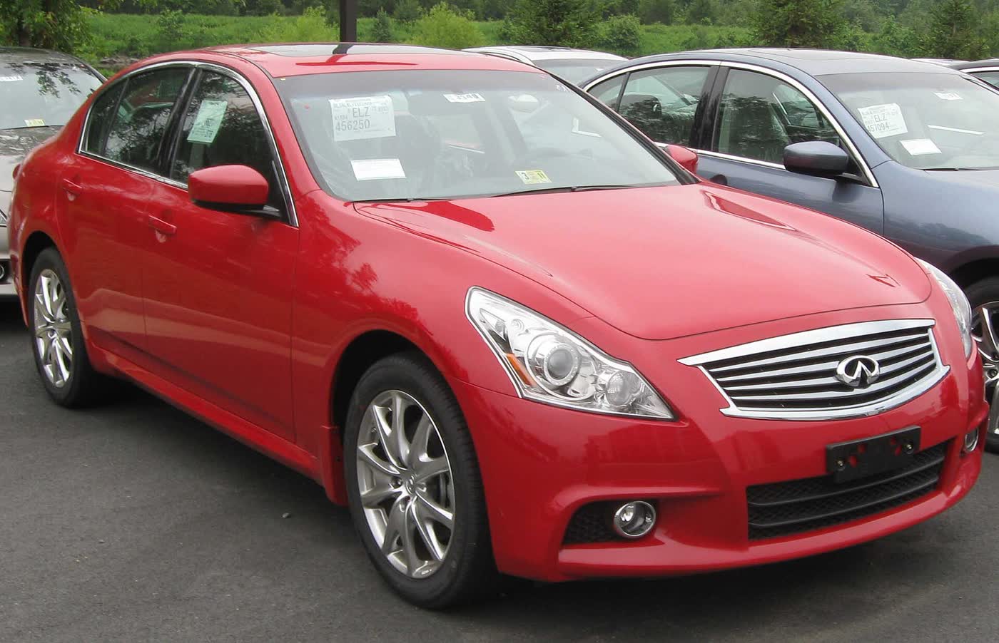 A red 2010 Infiniti G37 sedan on a dealer lot with stickers in the glass