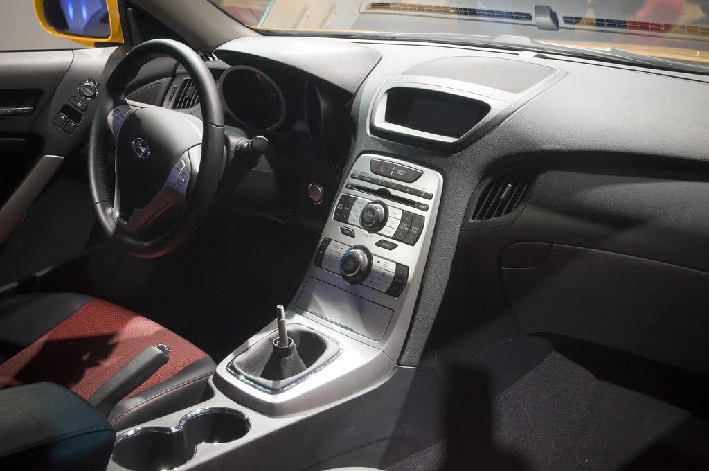 The interior of a Hyundai Genesis Coupe, showing the centre stack, manual shifter and red and black seats