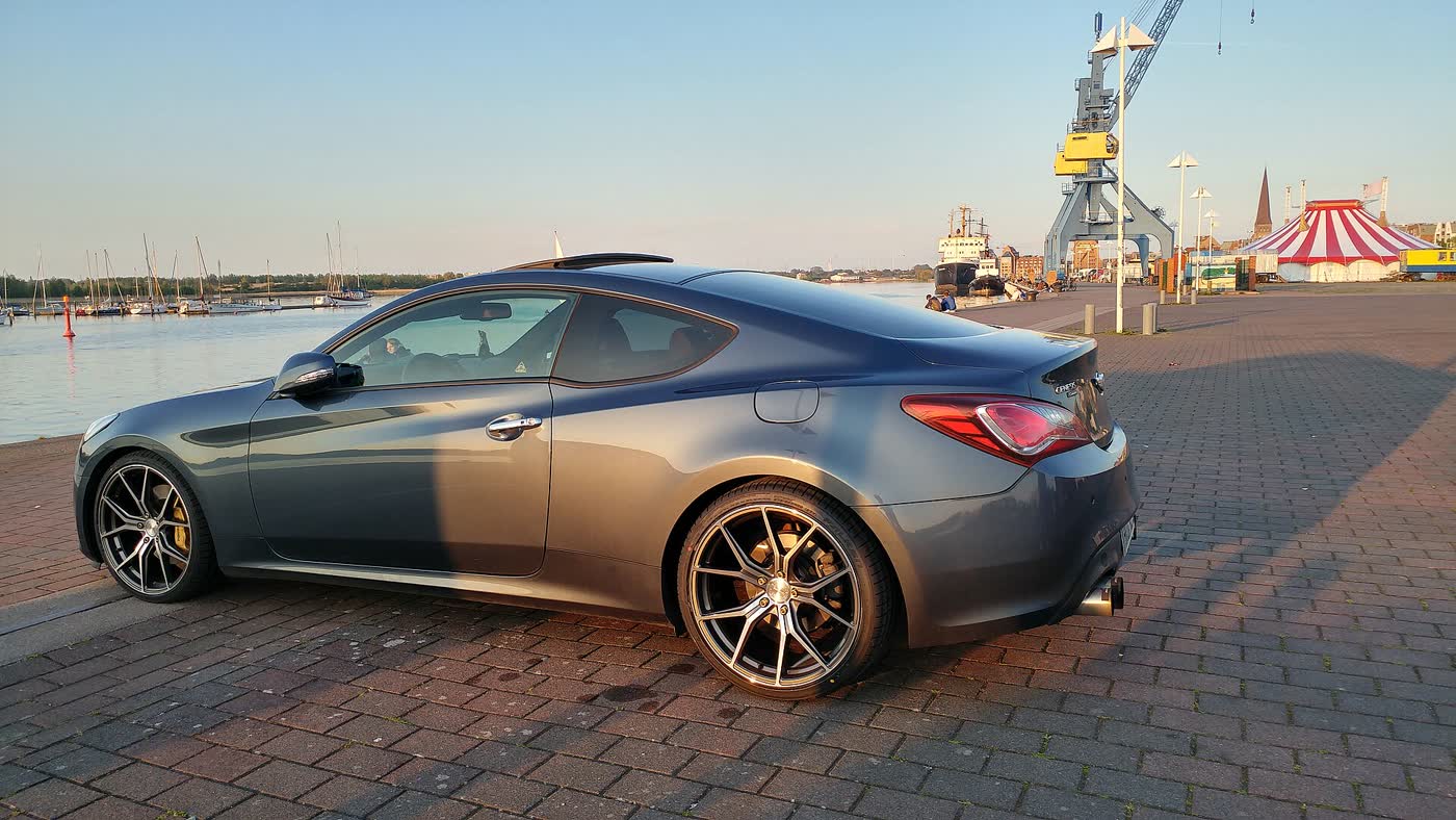 A grey facelift Hyundai Genesis Coupe lowered on aftermarket wheels, parked at a harbour