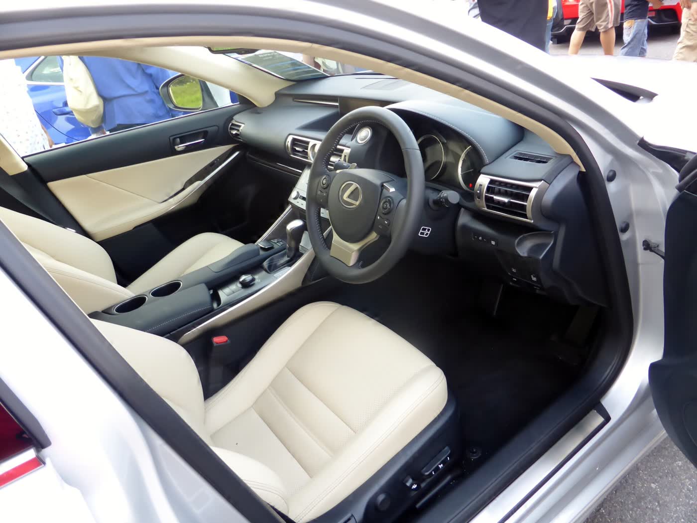 The front cabin of a right-hand-drive Lexus IS 350 with cream leather seats, a dark dashboard, a click-style controller on the centre console and a central display