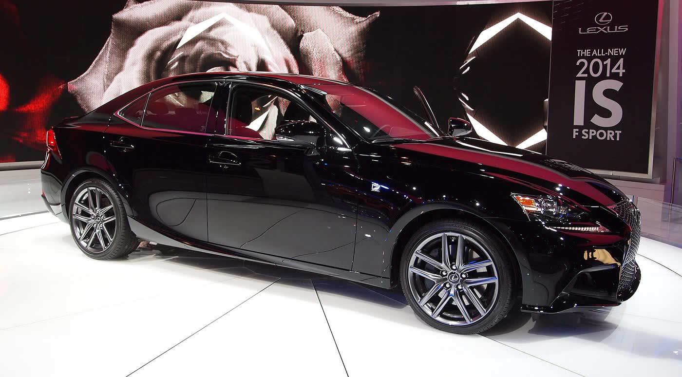 A black Lexus IS 350 F Sport sedan in profile on a white show floor, with its multi-spoke alloy wheels and a sign reading The all-new 2014 IS F Sport behind it