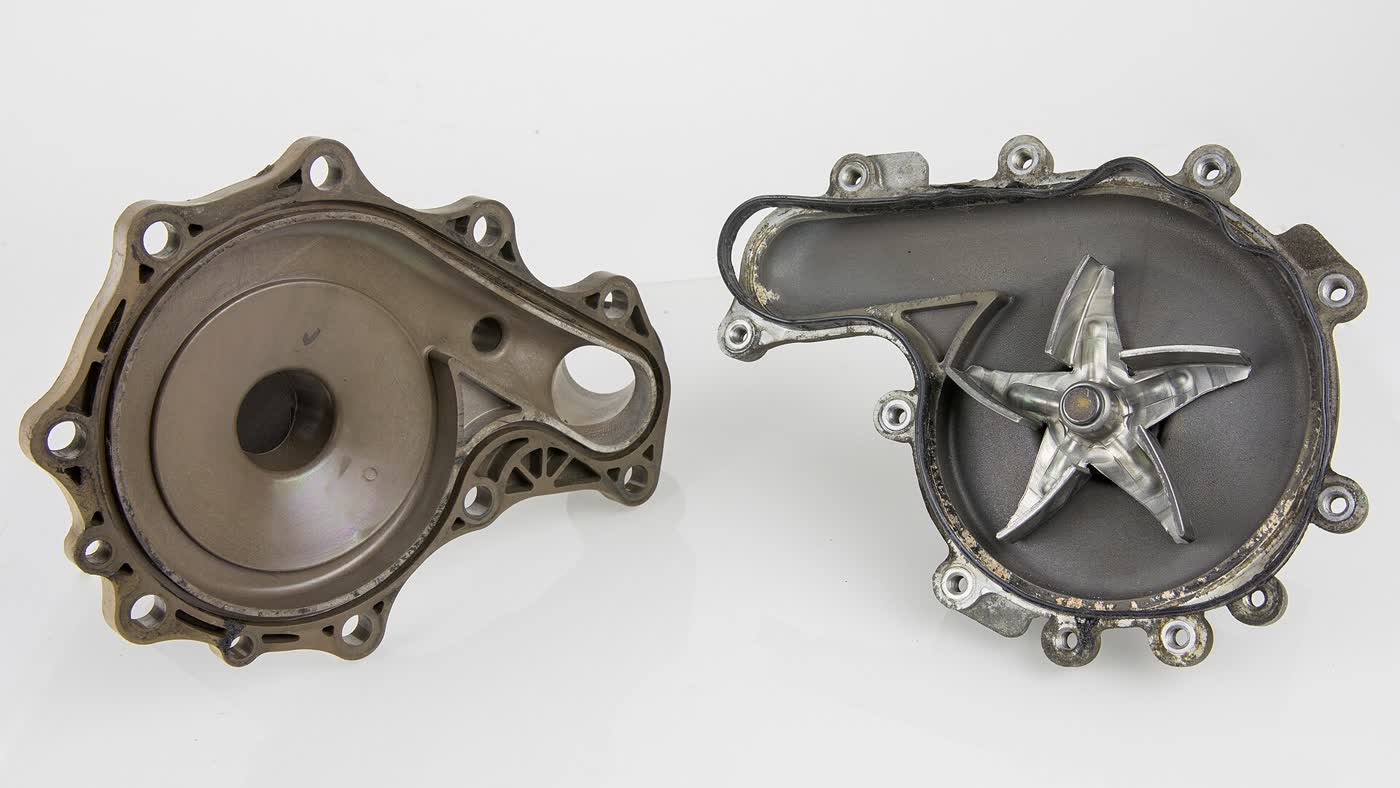 An opened automotive coolant pump on a white background: the empty cast housing on the left and the other half on the right showing a five-bladed metal impeller