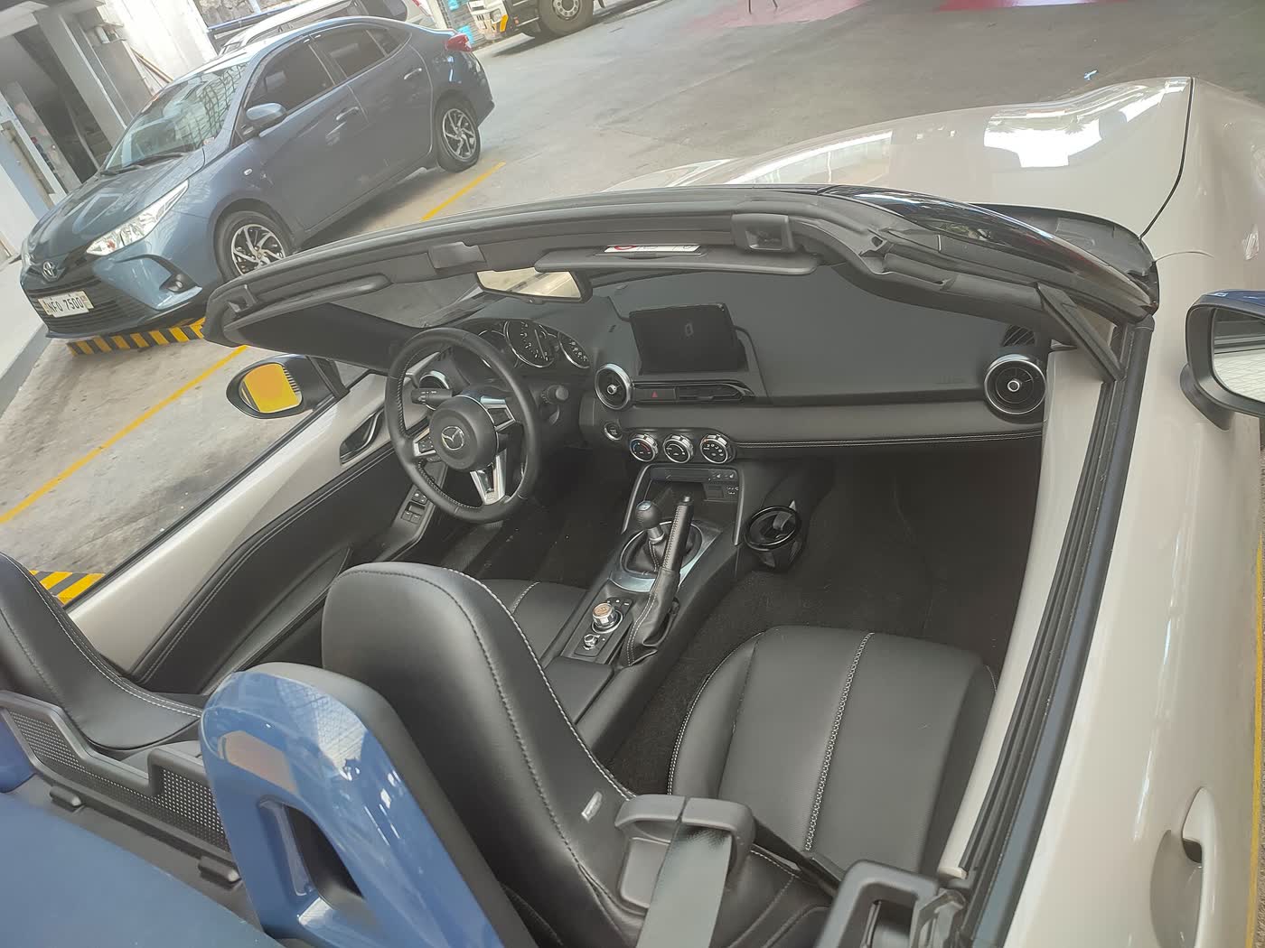 The interior of a Mazda MX-5 ND, showing the manual shifter, black leather seats and centre screen