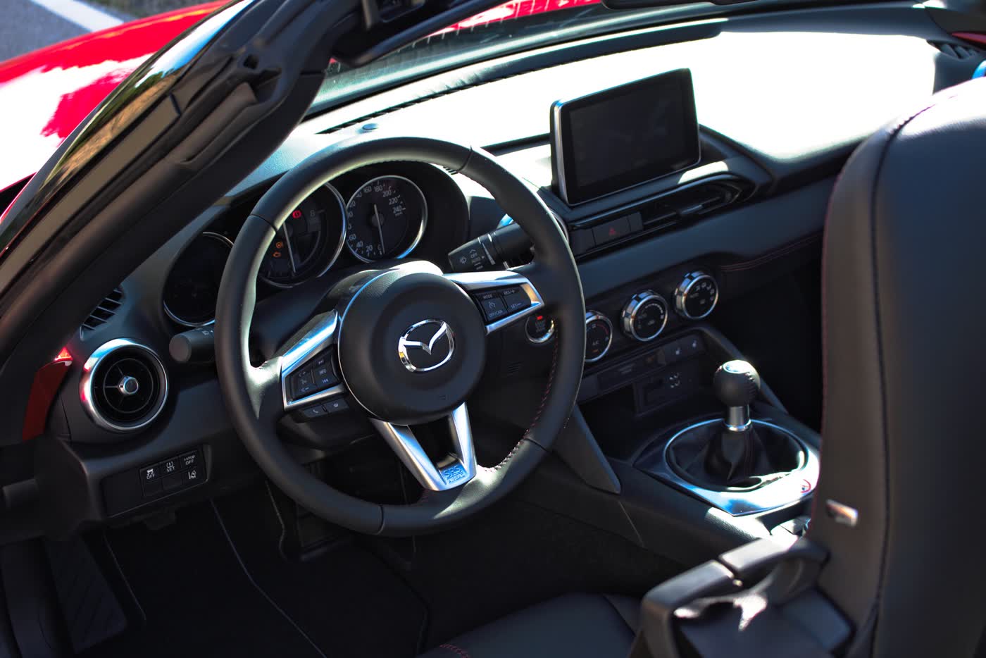 The cockpit of an early Mazda MX-5 ND, with the centre infotainment screen, gauges and shifter in view
