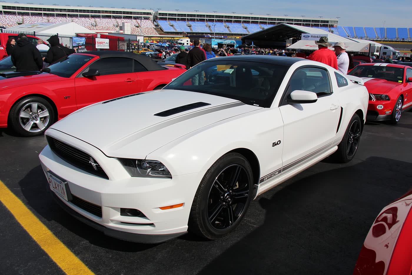 A white 2013 Ford Mustang GT California Special in a speedway car corral, 5.0 badge on the fender