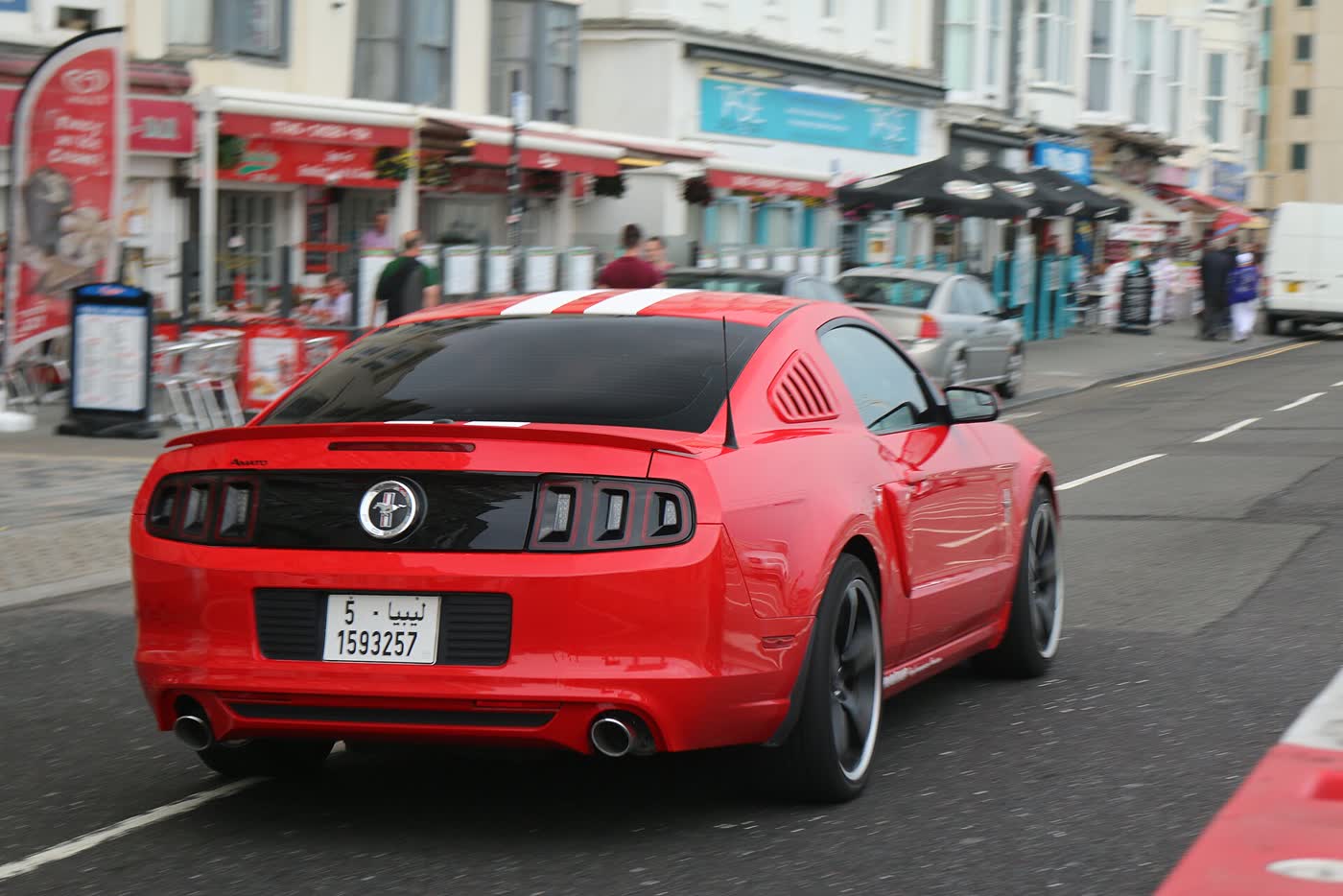 A red Ford Mustang S197 facelift driving away along a street, seen from behind