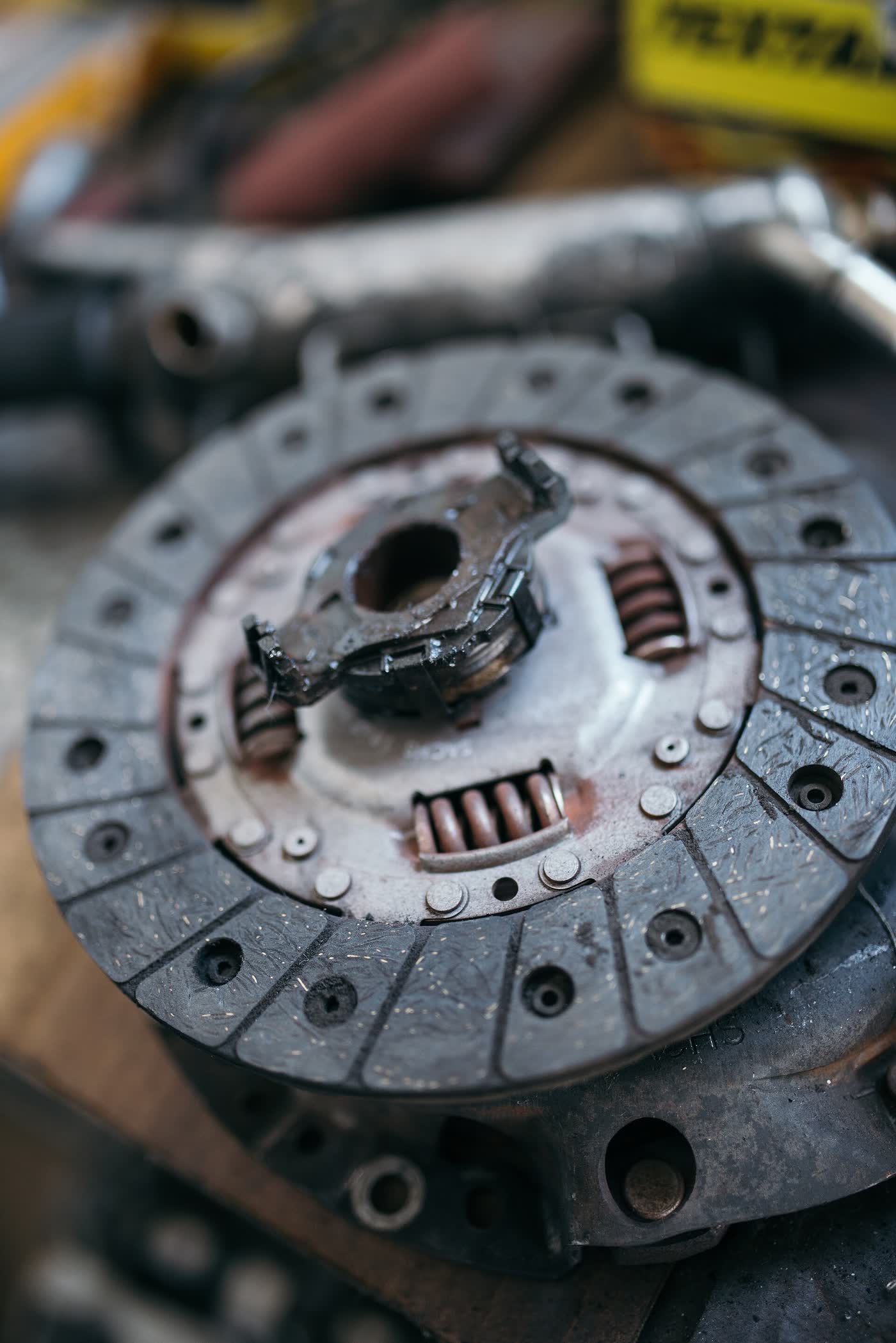 A worn clutch disc lying among tools on a workshop bench