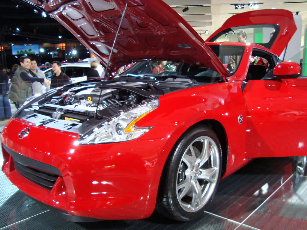 A red Nissan 370Z with its bonnet raised at a motor show, the VQ37 V6 visible