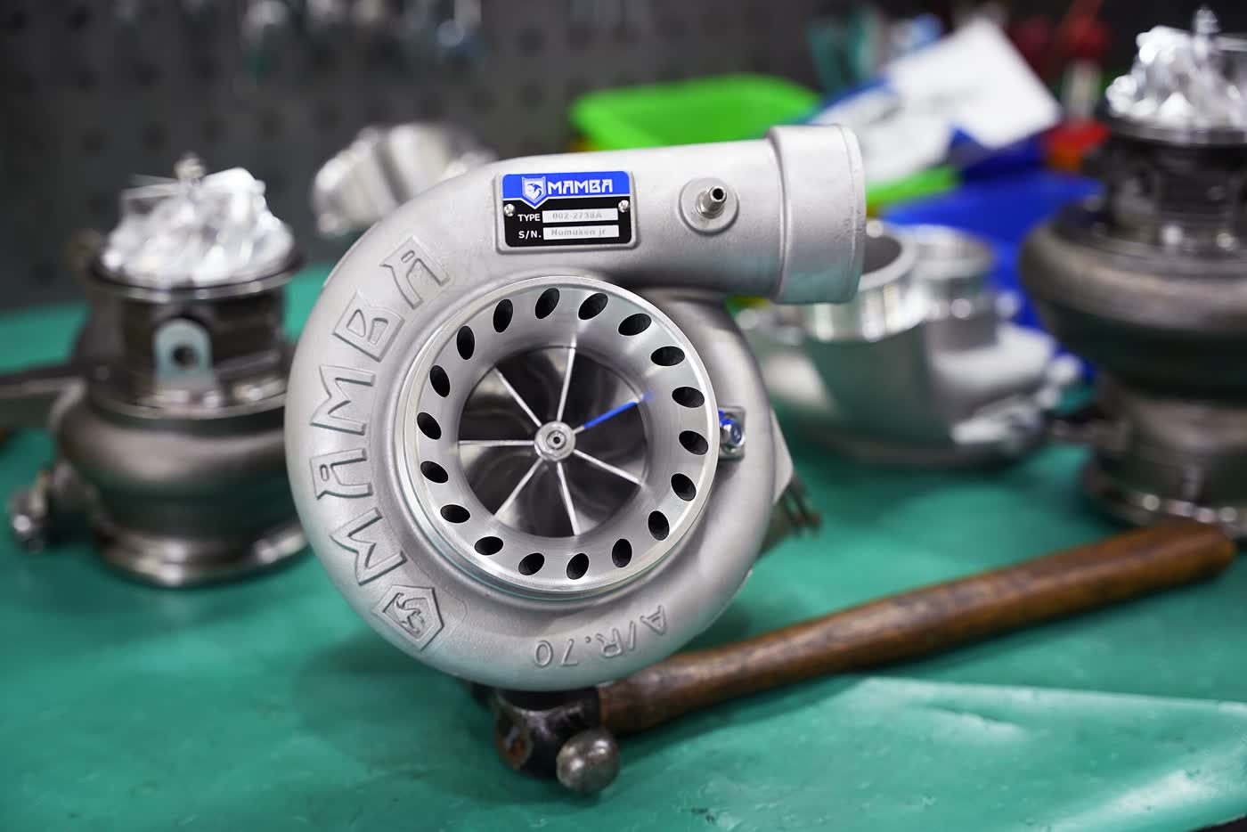 A turbocharger on a workbench with its compressor wheel visible, two more units beside it