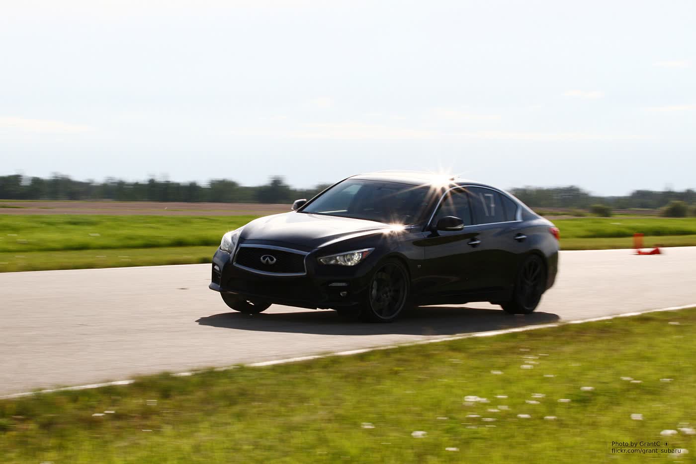 A black Infiniti Q50 sedan cornering on an autocross course, with an orange cone behind it