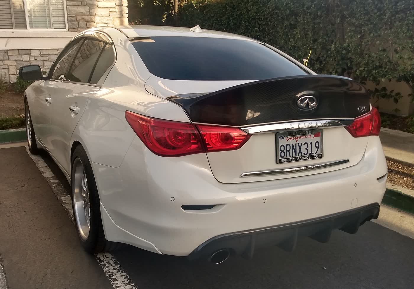 The rear of a white Infiniti Q50 sedan with a carbon-fibre trunk lid, a rear diffuser and aftermarket wheels