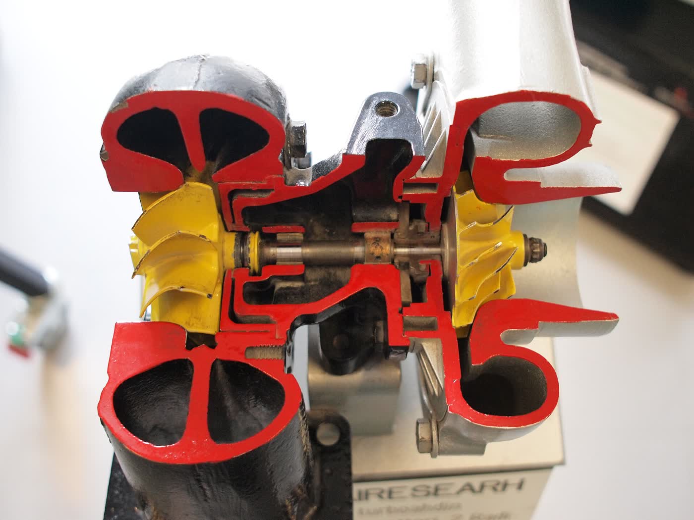 A turbocharger cut in half and painted red at the cut, showing the turbine wheel, the compressor wheel and the shaft and bearing housing between them