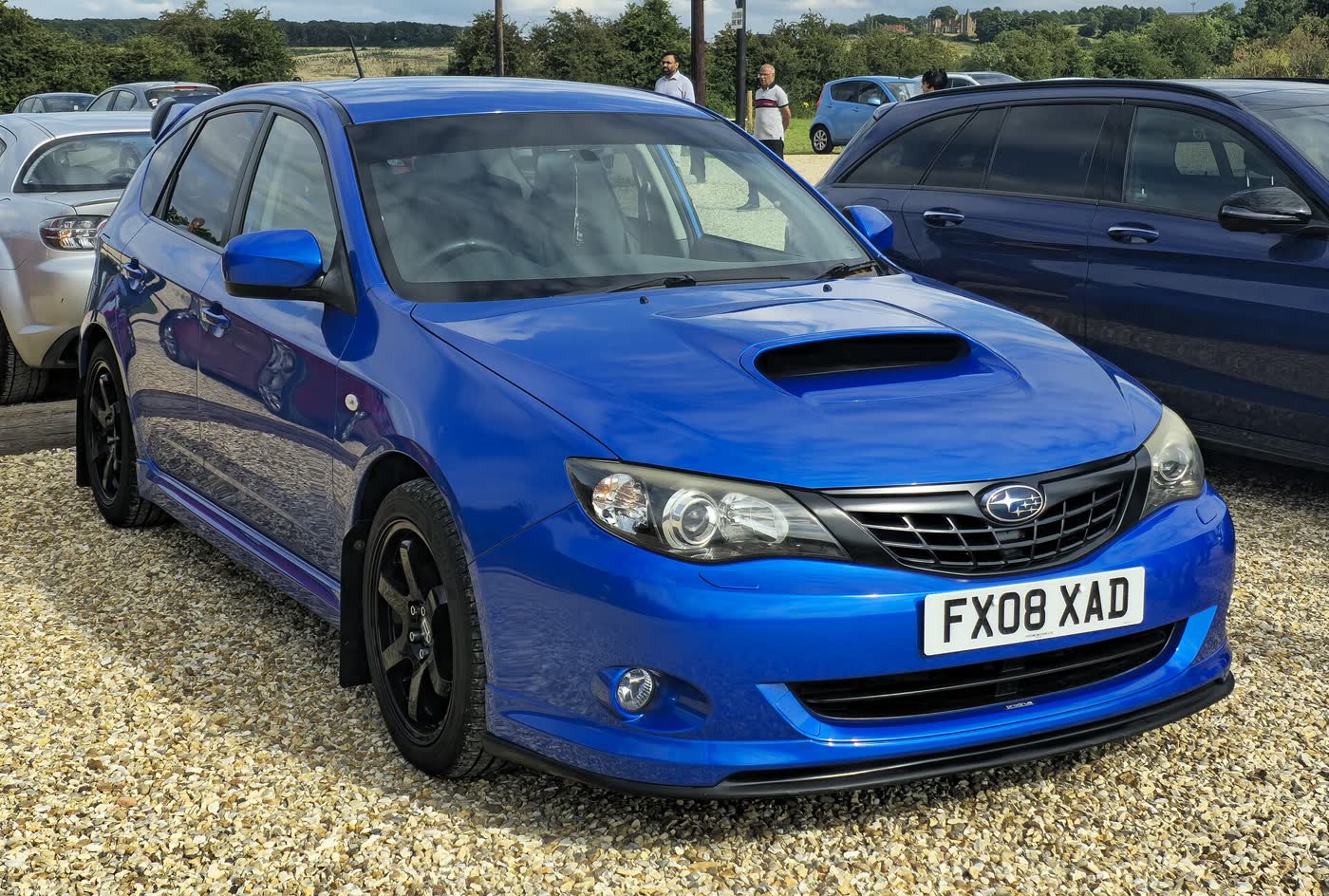 A Subaru Impreza WRX hatchback parked on grass, three-quarter view