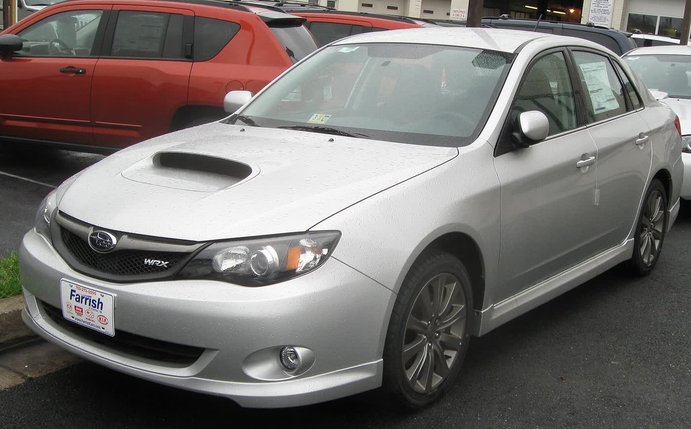 A silver 2009 Subaru Impreza WRX sedan on a dealer lot, front three-quarter view, with the WRX badge on the grille and the bonnet scoop visible