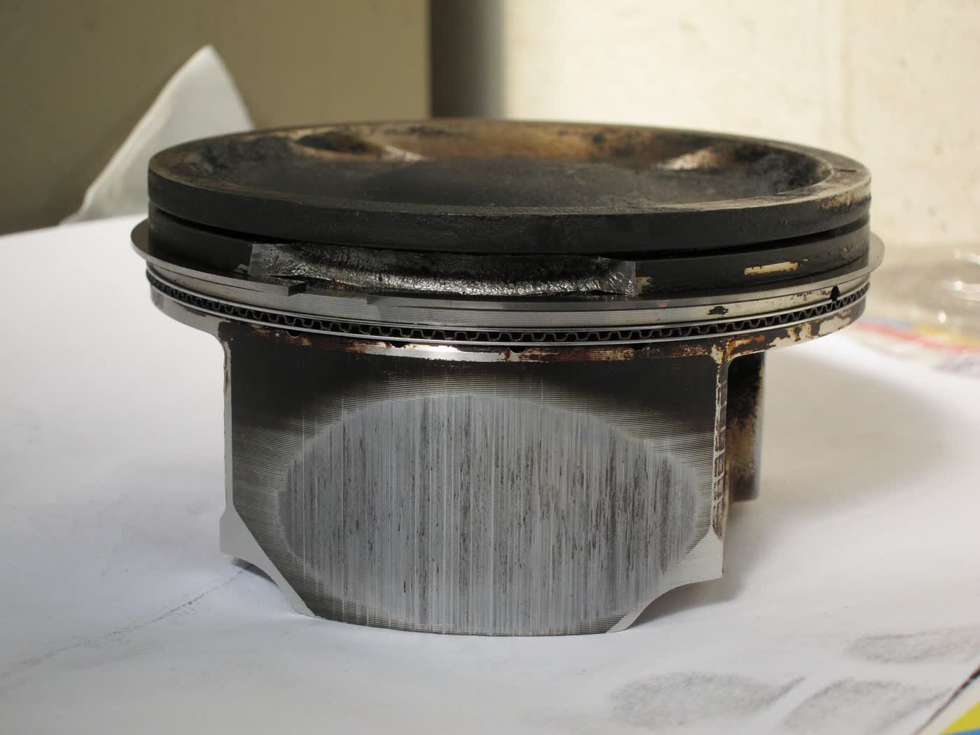 A badly scored piston removed from a Subaru Impreza boxer engine, with damage around the ring lands and skirt